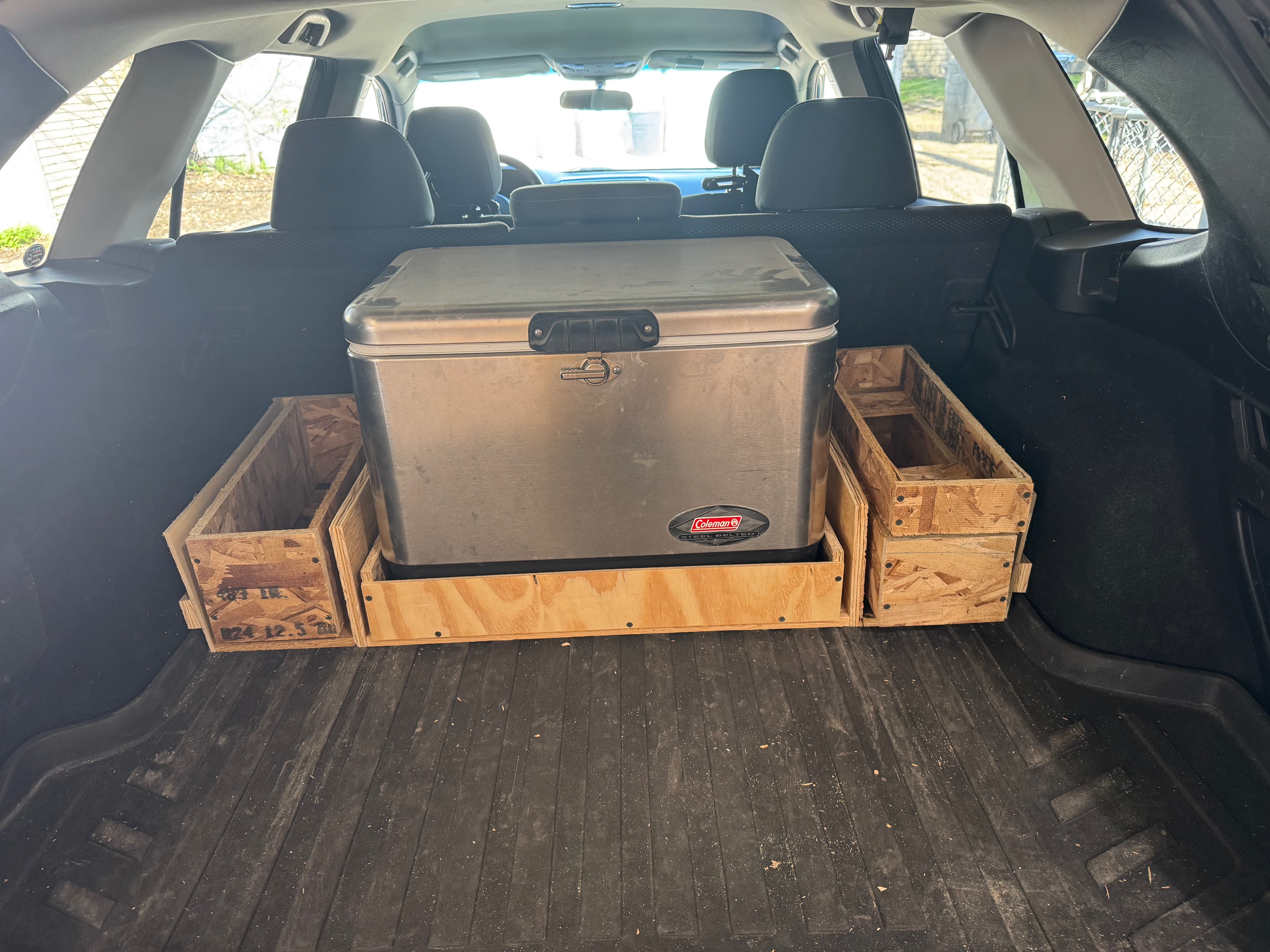The back of an SUV with a Coleman cooler and two crates in the trunk.