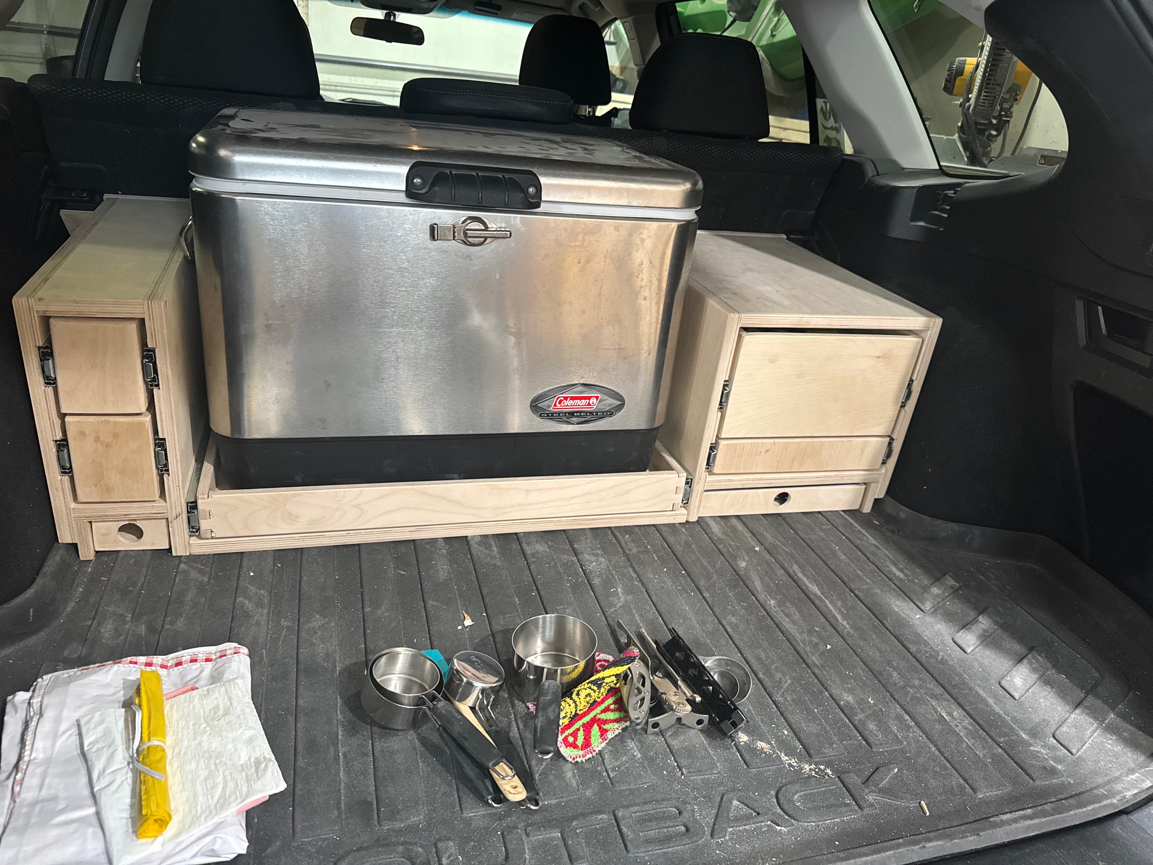 The back of an SUV with a Coleman cooler and various camping supplies on display.