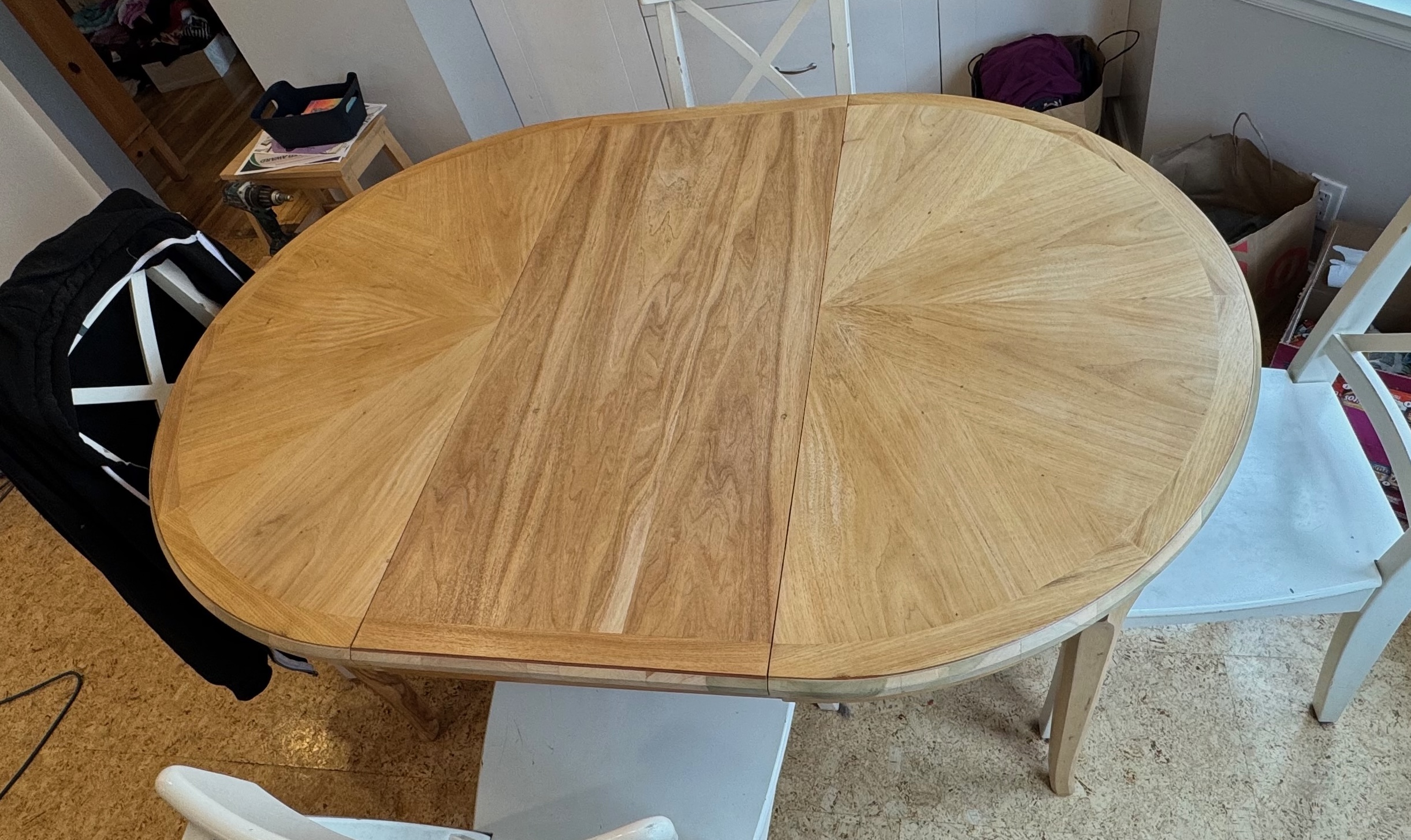 An oval wooden dining table with three white chairs pushed in around it.